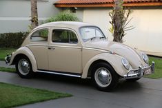 an old vw bug is parked in front of a house with palm trees and grass