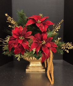 a gold vase filled with red poinsettia and greenery on top of a table