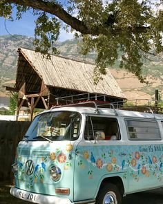 an old vw bus parked in front of a wooden building with flowers painted on the side