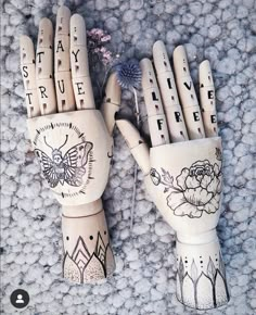 two wooden hand sculptures with words written on them and flowers in the middle one is made out of wood