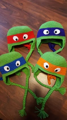 three crocheted hats with googly eyes are on top of a wooden table