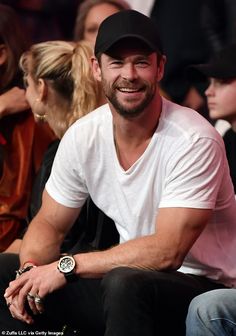 a man sitting in front of a crowd wearing a black hat and white t - shirt