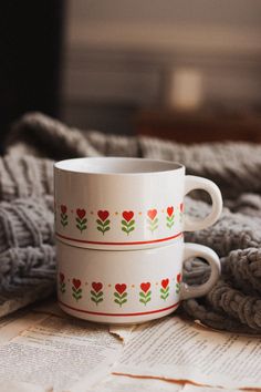 two coffee mugs sitting next to each other on top of a table covered in blankets