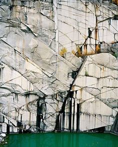 a large rock formation next to a body of water with trees growing out of it