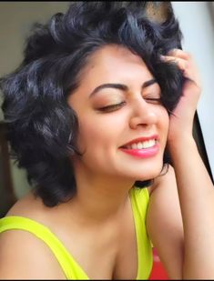 a close up of a person wearing a yellow shirt and smiling with her hair in the air