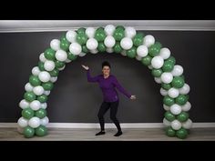 a woman standing in front of a green and white arch with balloons on the side