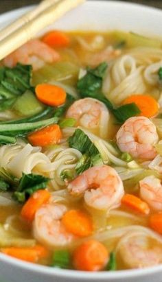 a bowl of shrimp noodle soup with carrots and spinach on the side