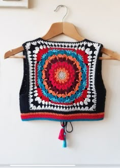 a crocheted sweater hanging on a wall with a wooden hanger in front of it