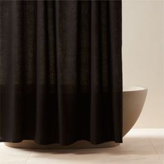 a black and white shower curtain in front of a bathtub with a bowl on the floor