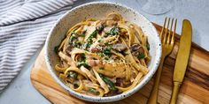 a white bowl filled with pasta and mushrooms on top of a wooden cutting board next to silverware