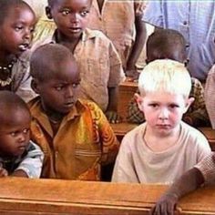 a group of young children sitting in front of a wooden desk with one boy looking at the camera