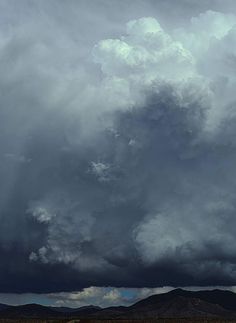 an airplane is flying in the sky with dark clouds above it and mountains behind it