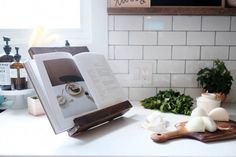 an open book sitting on top of a kitchen counter next to garlic and other ingredients