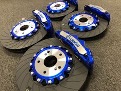 four blue brake discs and rotors on top of a gray carpeted flooring area