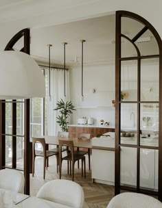 an open kitchen and dining room area with white walls, wood flooring and large arched windows