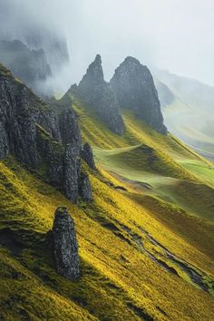 the mountains are covered in green grass and rock formations, with fog rolling over them