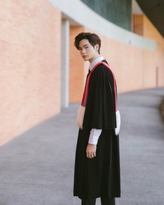 a young man standing in front of a building wearing a graduation gown and holding his hand on his hip