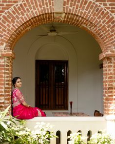 a woman in a pink sari sitting on the ledge of a brick building with an arched doorway