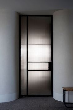 an empty room with a bench in front of the door and light coming through it