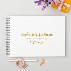 a spiral notebook with gold foil lettering on the cover next to a pair of scissors