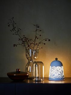 two vases with flowers in them sitting on a table next to a bowl and lamp