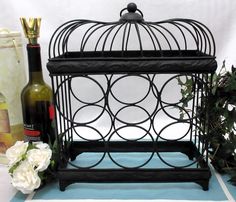 a birdcage with wine bottles and flowers next to it on a blue mat