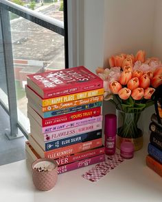 a stack of books sitting on top of a table next to a vase filled with flowers