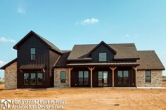 a large black house sitting in the middle of a dirt field with lots of windows