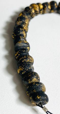 a black and gold bead necklace on a white surface with a hook in the middle