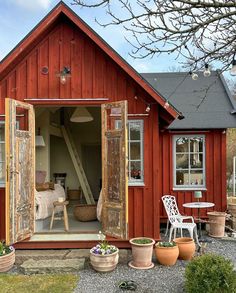 a small red house with an open door and some chairs in front of the building