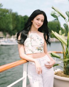 a woman standing on the deck of a boat next to a potted plant and looking at the camera