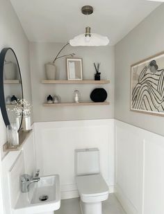 a white toilet sitting in a bathroom next to a sink under a mirror and shelf