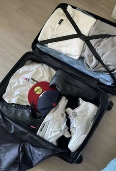 an open suitcase with clothing and shoes in it on the floor next to a bag