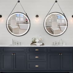 two round mirrors are hanging above the double sink vanity in this modern bathroom with white walls and blue cabinetry