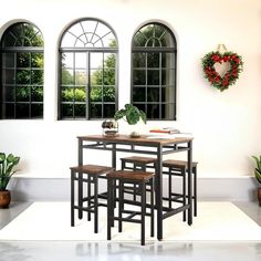 a table and four stools in front of three windows with wreath on the wall