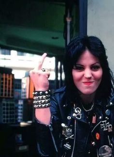 a woman with black hair and piercings making the peace sign while sitting in front of a table