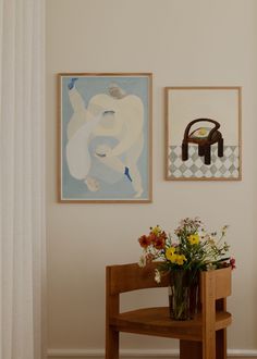 two paintings hang on the wall above a wooden table with flowers in front of it