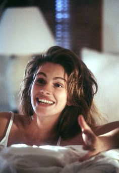 a woman laying on top of a bed with her hand up to the side and smiling