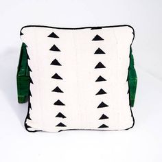 a white and green pillow with black triangles on the front, sitting on a white surface