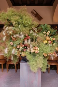 A stunning floral centerpiece featuring a smoke tree, roses, and grasses. The arrangement is displayed on a pedestal and adds a touch of elegance and drama to the surrounding tables. Modern Carnation Arrangements, Statement Flowers Wedding, Massive Flower Arrangements, Large Floral Installations, Modern Wedding Flower Arrangements, Artistic Flower Arrangements, Unique Wedding Florals, Ground Floral Arrangements Wedding, Dried Flowers Wedding Centerpieces