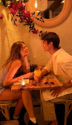 a man and woman sitting at a table with drinks in front of them, talking