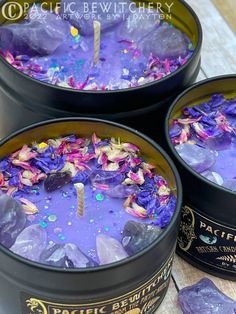 three tins filled with purple and pink flowers on top of a wooden table next to rocks