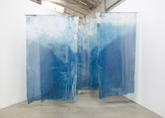 two blue curtains are hanging from the ceiling in an art gallery with white walls and concrete flooring