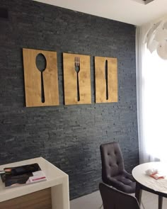 there is a table and chair in the room with three paintings on the wall behind it