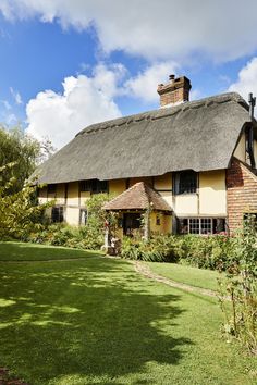 an old thatched roof house with green grass and trees in the foreground on a sunny day