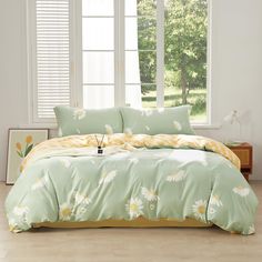 a bed with green and yellow comforters in front of a large window that has white flowers on it