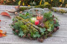 an arrangement of greenery and candles on a wooden table with autumn leaves around it