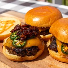 three hamburgers sitting on top of a wooden cutting board next to some onion rings