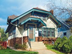 a house with green trim and brown shingles on the front porch, next to a sidewalk