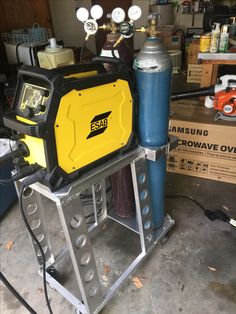 a yellow and black device sitting on top of a metal stand next to a blue cylinder